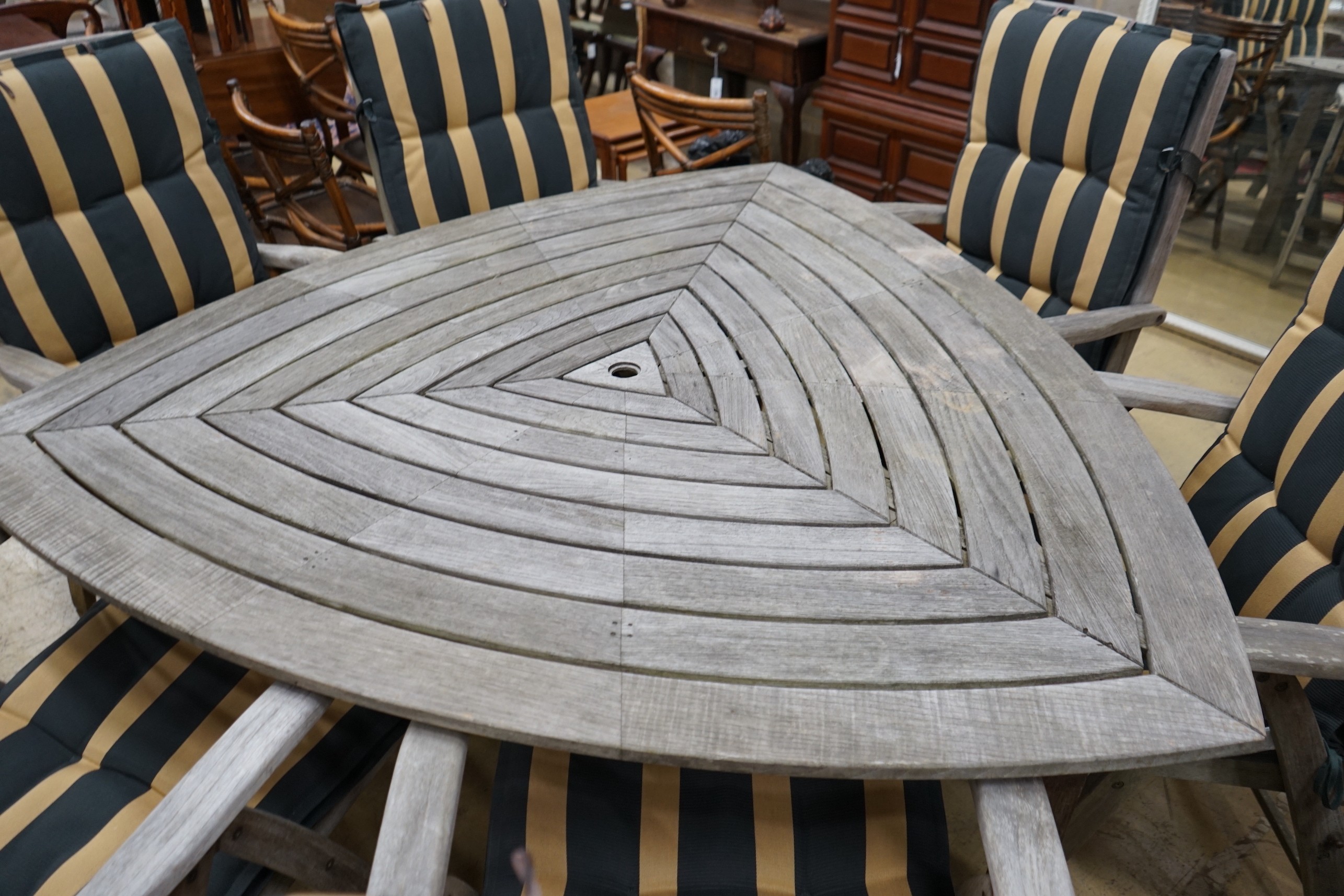 A Hartman weathered teak triangular garden table, width 170cm, height 76cm, six folding armchairs with seat pads and a tray top side table.